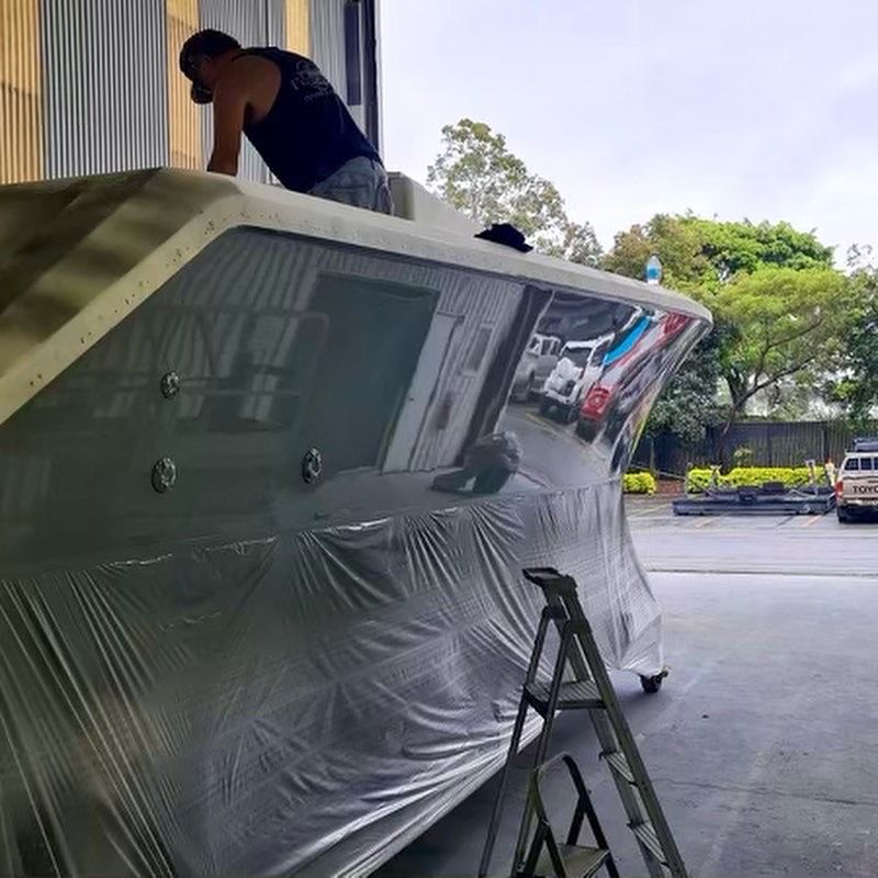 A crew member cutting and polishing the hull side of a motor yacht on the hardstand
